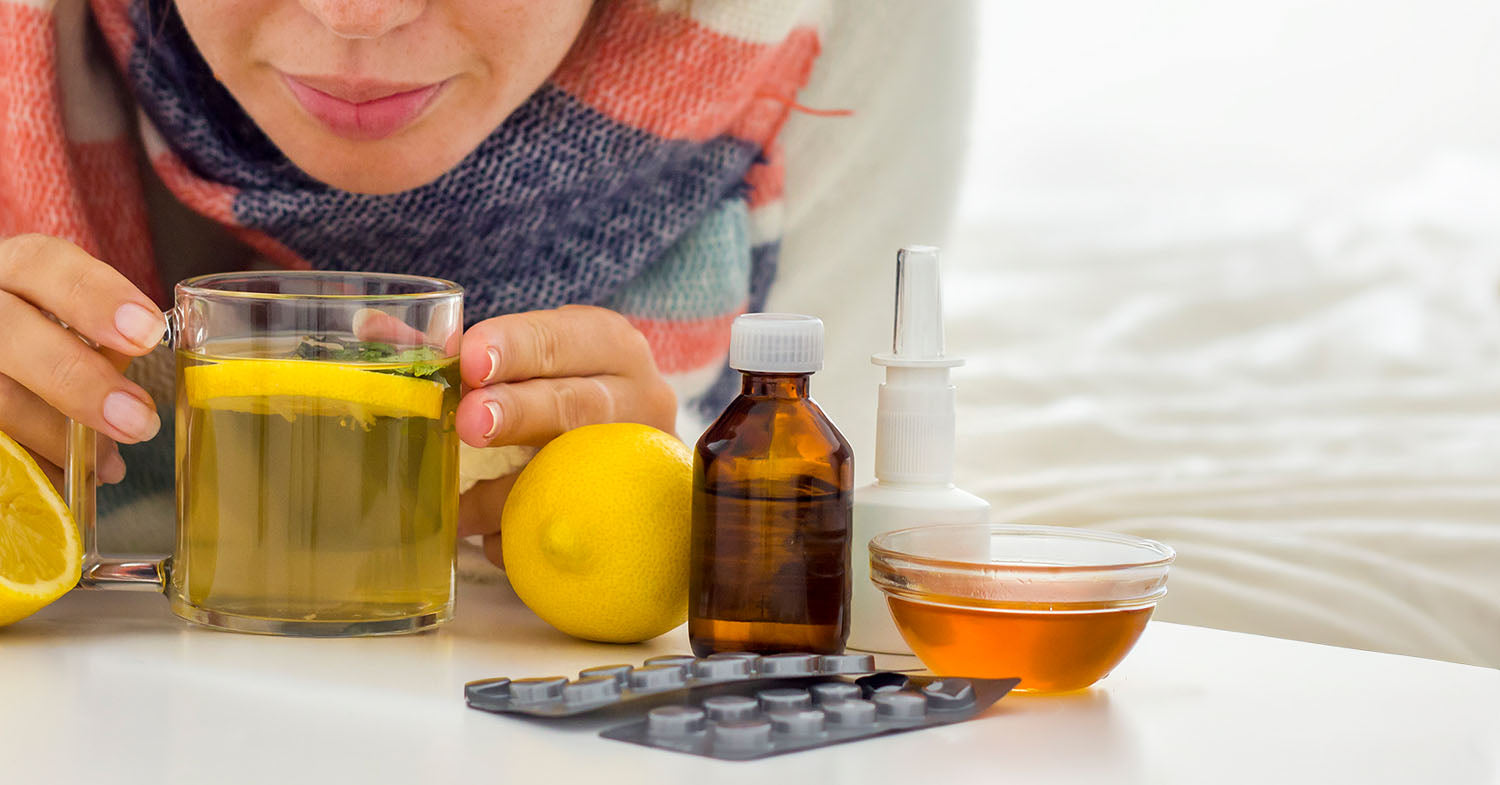 Cold and flu season essentials including tea, lemons, honey, and over-the-counter remedies on a bedside table.