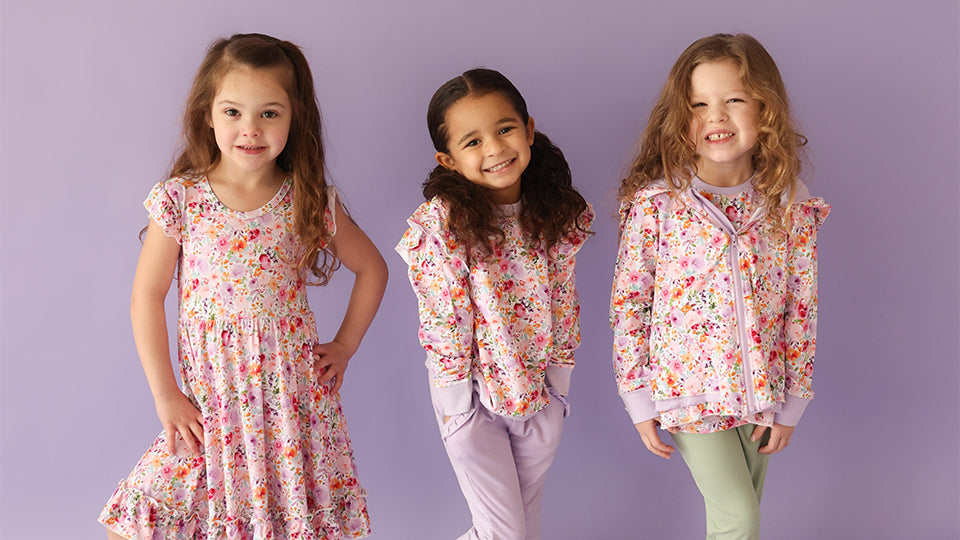 Three young girls modeling floral bamboo dresses, sweatshirts, and leggings from Autumn Moon Kids’ Clothing
